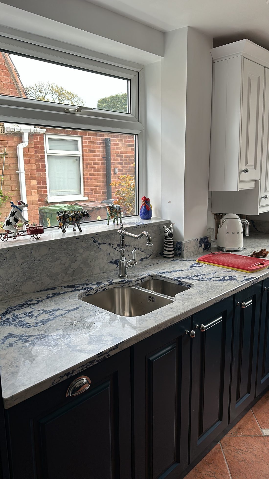 The same navy shaker kitchen from the worktop up — chrome tapware, an undermount sink and a bold blue-and-white marbled stone surface catching the light.